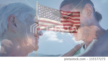 Smiling mother and son standing face to face on hilltop, with fluttering American flag on flagpole Smiling mother and son standing face to face on hilltop, with fluttering American flag on flagpole 135577273