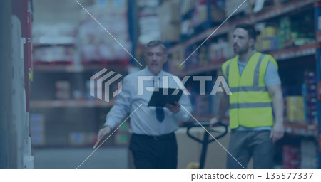 Manager in shirt and tie walking warehouse bay checking clipboard, worker operating pallet jack Manager in shirt and tie walking warehouse bay checking clipboard, worker operating pallet jack 135577337