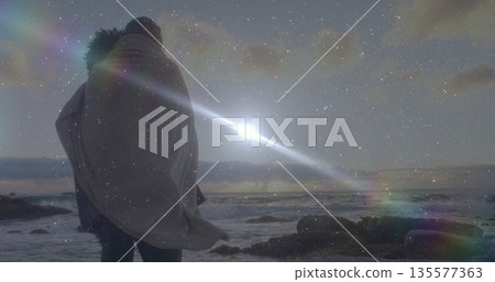 Standing couple wrapping in blanket on rocky shoreline, with ocean waves and lens flare, copy space Standing couple wrapping in blanket on rocky shoreline, with ocean waves and lens flare, copy space 135577363