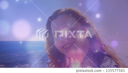 Kneeling woman gazing toward sea horizon on sea shore, with patterned top, bokeh lights, copy space 135577381