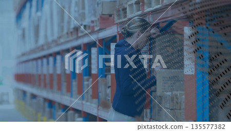 Leaning warehouse supervisor wearing suit inspecting box in warehouse, with metal racks, copy space Leaning warehouse supervisor wearing suit inspecting box in warehouse, with metal racks, copy space 135577382