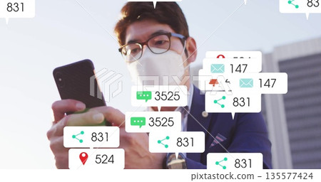 Masked Asian businessman holding smartphone, viewing alerts in business plaza, with chat overlays Masked Asian businessman holding smartphone, viewing alerts in business plaza, with chat overlays 135577424