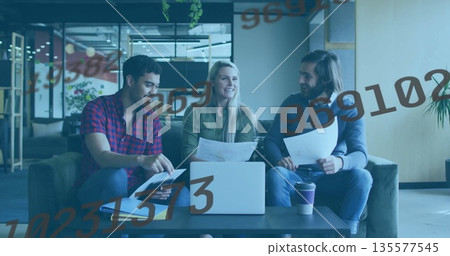 Collaborating professionals reviewing documents on laptop in office lounge on sofa, with coffee cup 135577545