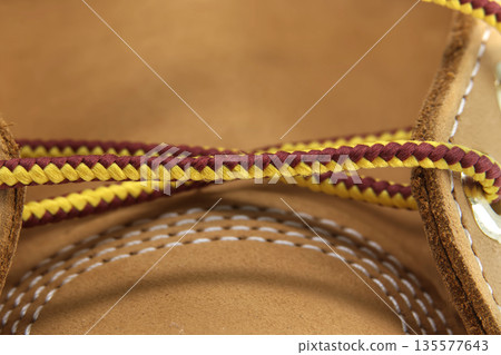 Close-up macro shot of braided yellow and burgundy shoelaces on a tan leather boot 135577643