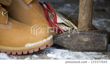 Work boots and sledgehammer resting on snowy ground, ready for winter labor Work boots and sledgehammer resting on snowy ground, ready for winter labor 135577645