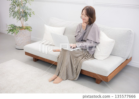 A happy senior woman working on a computer in the living room. Image of making reservations and applications. 135577666