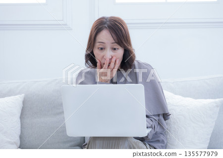 A senior woman using a computer is surprised and wonders if it's a scam. 135577979