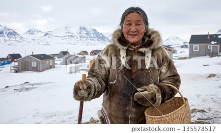 Elderly Inuit woman in traditional fur clothing holding a basket in a snowy Arctic village 135578517