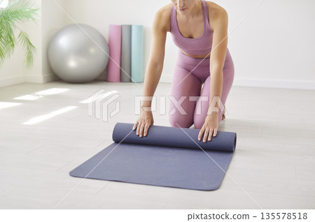 Woman preparing for fitness as she rolls a yoga mat in bright home studio space 135578518