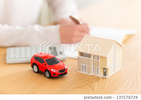 中年婦女的手拿著家庭帳簿，旁邊是房子和汽車。 135578729