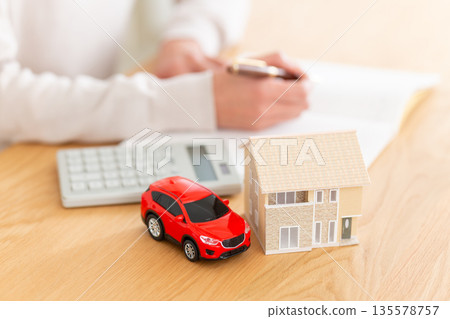 Middle-aged woman's hand with household account book, house and car 135578757