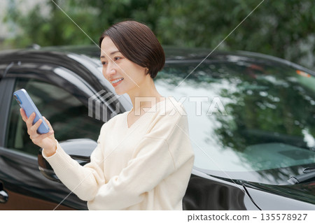 一名女子在車前操作智慧型手機 一名女子在車前操作智慧型手機 135578927