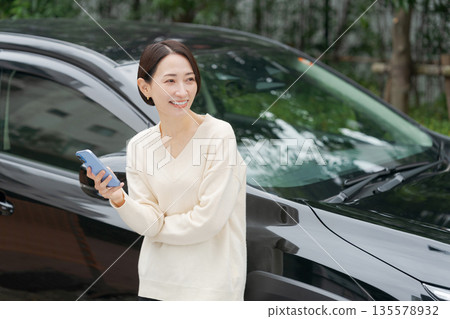 A woman operating a smartphone in front of a car 135578932