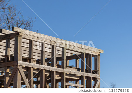 Timber frame construction rises with wooden scaffolding under a bright blue sky Timber frame construction rises with wooden scaffolding under a bright blue sky 135579358