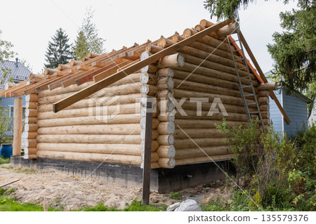 A partially built log cabin sits on a concrete foundation in a yard A partially built log cabin sits on a concrete foundation in a yard 135579376