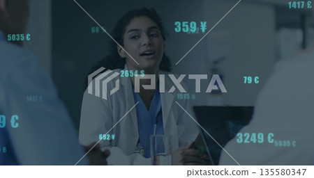 Female doctor in blue scrubs with stethoscope leading meeting in hospital room, currency overlays Female doctor in blue scrubs with stethoscope leading meeting in hospital room, currency overlays 135580347