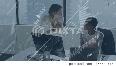 Discussing data analysis two women in business casual at office, with monitor laptop documents Discussing data analysis two women in business casual at office, with monitor laptop documents 135580357