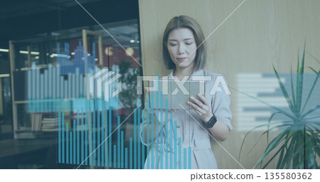 Holding tablet, Asian executive in blazer viewing chart overlay at glass partition, copy space Holding tablet, Asian executive in blazer viewing chart overlay at glass partition, copy space 135580362