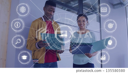 Reviewing documents two workers holding colored files in office with ductwork and digital overlay Reviewing documents two workers holding colored files in office with ductwork and digital overlay 135580380