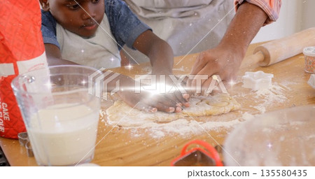 Father and son in aprons kneading dough on kitchen countertop, with rolling pin and sprinkles Father and son in aprons kneading dough on kitchen countertop, with rolling pin and sprinkles 135580435
