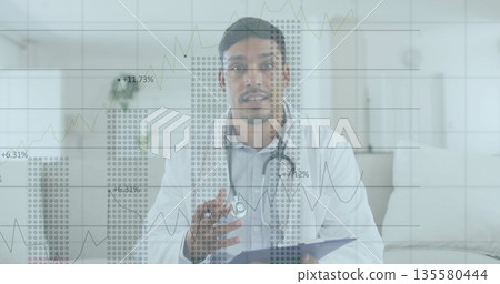 Showing South Asian doctor gesturing at home, with clipboard pen stethoscope and data charts 135580444