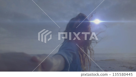 Holding partner hand, woman wearing denim shirt walking along sandy shore, sun flare sparkling Holding partner hand, woman wearing denim shirt walking along sandy shore, sun flare sparkling 135580445