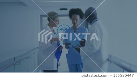 Reviewing paperwork staff wearing lab coats with blue folders in hospital corridor with door emblem Reviewing paperwork staff wearing lab coats with blue folders in hospital corridor with door emblem 135580447