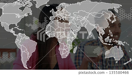 Smiling colleagues wearing business attire holding white mugs at wood table, featuring map overlay 135580466