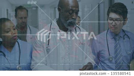 Walking medical team reviewing medical records in hospital corridor, with tablet, stethoscopes 135580541