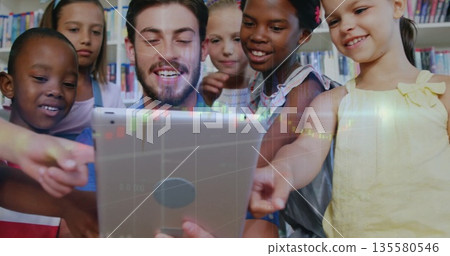 Guiding male tutor showing children data overlay on tablet at library table, with colorful shelves Guiding male tutor showing children data overlay on tablet at library table, with colorful shelves 135580546
