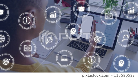 Man wearing mustard sweater holding phone, viewing laptop screen in office, data icons, copy space 135580552