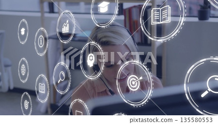 Focusing office worker wearing headset analyzing data on computer at desk, with digital icons Focusing office worker wearing headset analyzing data on computer at desk, with digital icons 135580553