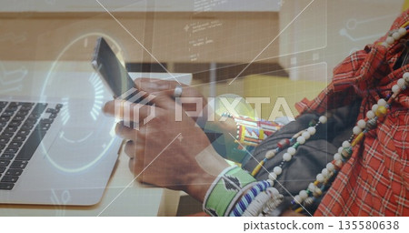 Man in red cloth and bracelets holding smartphone at wooden desk, with laptop and digital overlay Man in red cloth and bracelets holding smartphone at wooden desk, with laptop and digital overlay 135580638