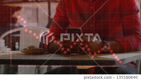 Holding smartphone man wearing red shirt at wooden table viewing downward trend graph with pastry 135580640