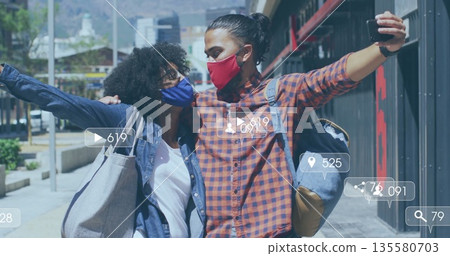 Pausing masked couple taking selfie with smartphone on downtown street, with backpack, tote bag Pausing masked couple taking selfie with smartphone on downtown street, with backpack, tote bag 135580703
