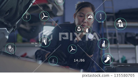 Female mechanic in coveralls and gloves inspecting engine under open hood in garage, with eco icons Female mechanic in coveralls and gloves inspecting engine under open hood in garage, with eco icons 135580705