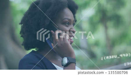 Smiling woman in navy blazer, white top, holding smartphone to ear in leafy garden, with wristwatch Smiling woman in navy blazer, white top, holding smartphone to ear in leafy garden, with wristwatch 135580706