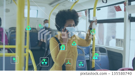 Talking commuter woman holding smartphone and yellow handrail inside city bus, with masked riders 135580740