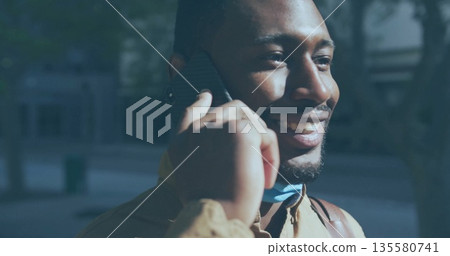 Smiling man talking on smartphone on city sidewalk, with backpack and surgical mask, copy space 135580741