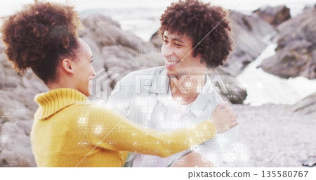 Laughing couple wearing mustard sweater and light grey shirt standing on rocky beach, with pebbles Laughing couple wearing mustard sweater and light grey shirt standing on rocky beach, with pebbles 135580767