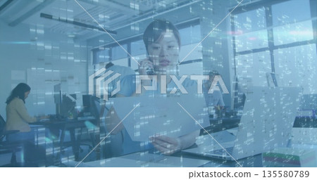 Woman holding documents and speaking on smartphone in open plan office with city skyline 135580789