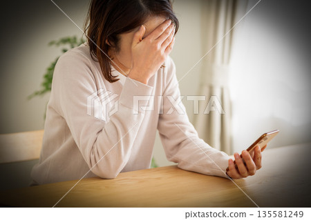 A middle-aged woman looking at her smartphone in her room and feeling depressed 135581249