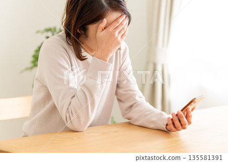 A middle-aged woman looking at her smartphone in her room and feeling depressed 135581391