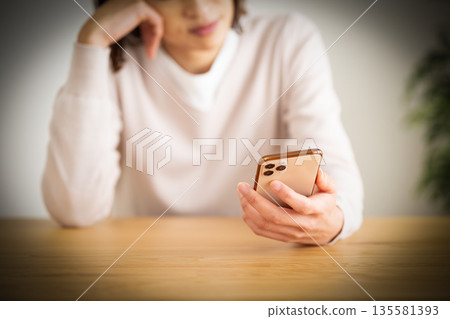 A middle-aged woman worried about her smartphone in her room A middle-aged woman worried about her smartphone in her room 135581393