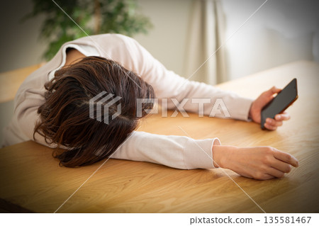 A middle-aged woman lazing around in her room looking at her smartphone 135581467