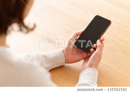 Middle woman looking at smartphone in room Middle woman looking at smartphone in room 135581583