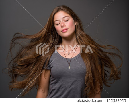 Long brown hair flowing mid movement, young woman with closed eyes, relaxed expression, casual gray shirt, studio portrait 135582055