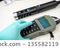 Close up of gloved hands pressing buttons on a portable pH meter during measurement. 135582119