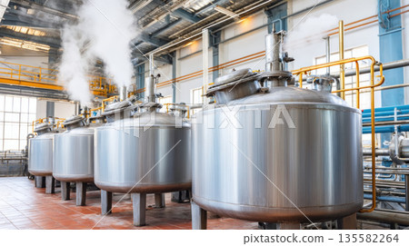 Large stainless steel tanks with steam in modern industrial facility, used for chemical or food processing production 135582264