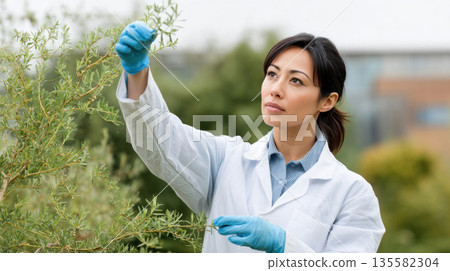 Scientist in white lab coat and blue gloves examining green plant outdoors, focused and thoughtful in natural environment 135582304